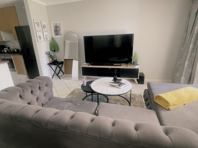 Open-plan living area featuring tiled flooring and an integrated kitchen with cabinetry, flowing into a lounge space with access to a balcony.