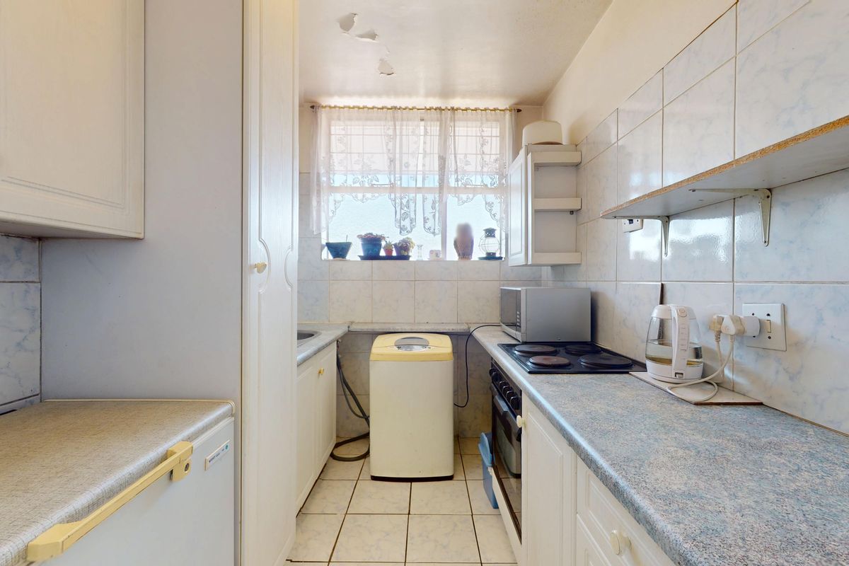 A compact, dated kitchen featuring built-in cabinetry, electric hob, oven, and tiled finishes, requiring cosmetic updates to modernize the space.