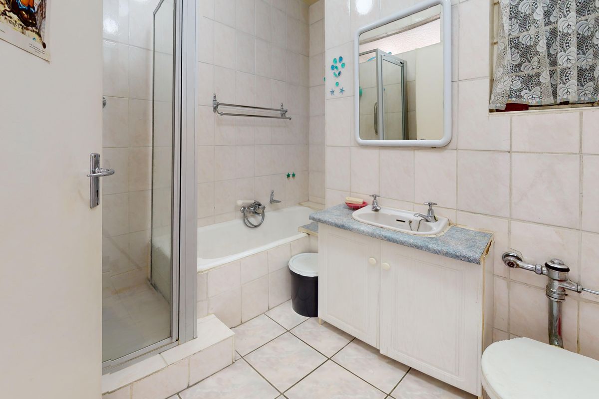 A functional bathroom featuring a shower enclosure, bathtub, vanity cabinet with basin, and tiled finishes throughout.