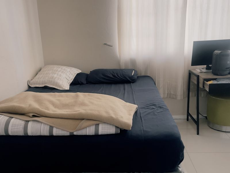 A simple bedroom featuring tiled flooring and natural light through window curtains.