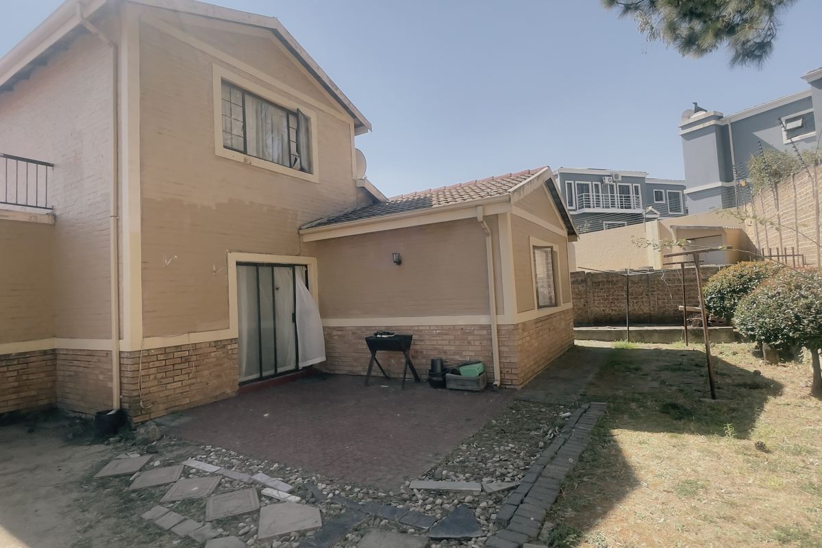 Rear view of a two-story apartment building featuring a paved patio area, brick exterior walls, and a private garden space.