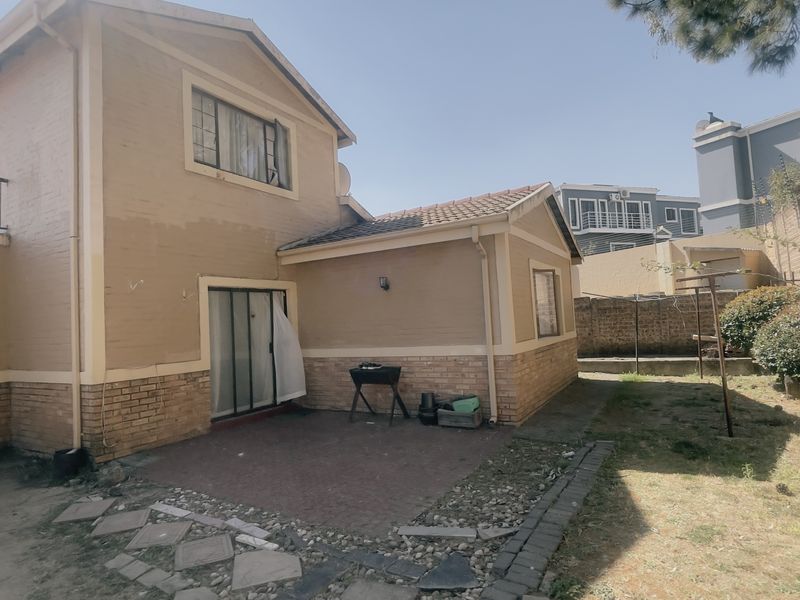Rear view of a two-story apartment building featuring a paved patio area, brick exterior walls, and a private garden space.