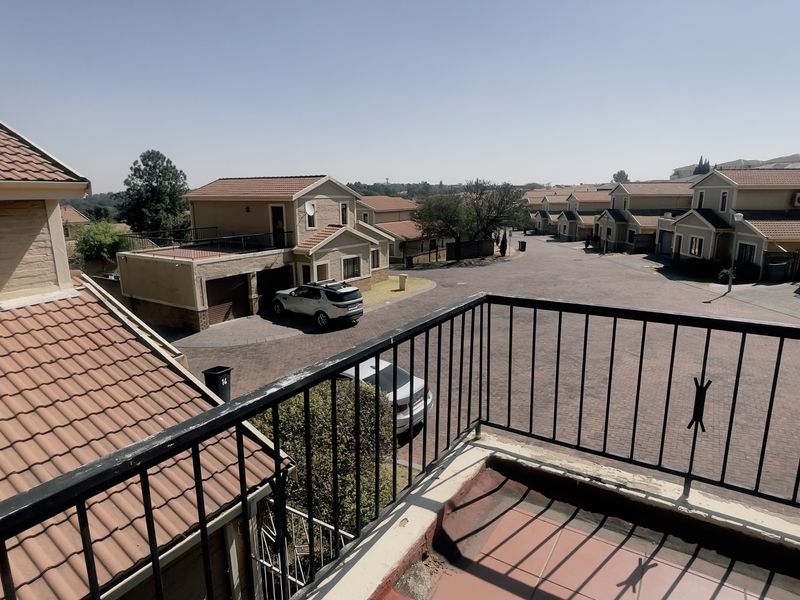 An elevated balcony with a metal balustrade overlooking the residential complex street and surrounding neighborhood.