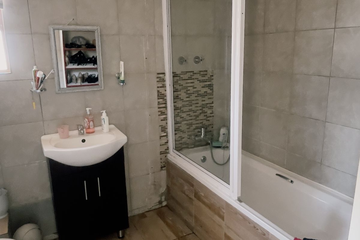 A functional bathroom featuring a vanity unit, a bathtub with a glass shower screen, and neutral wall and floor tiling.