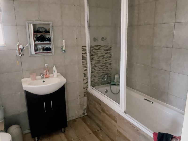 A functional bathroom featuring a vanity unit, a bathtub with a glass shower screen, and neutral wall and floor tiling.