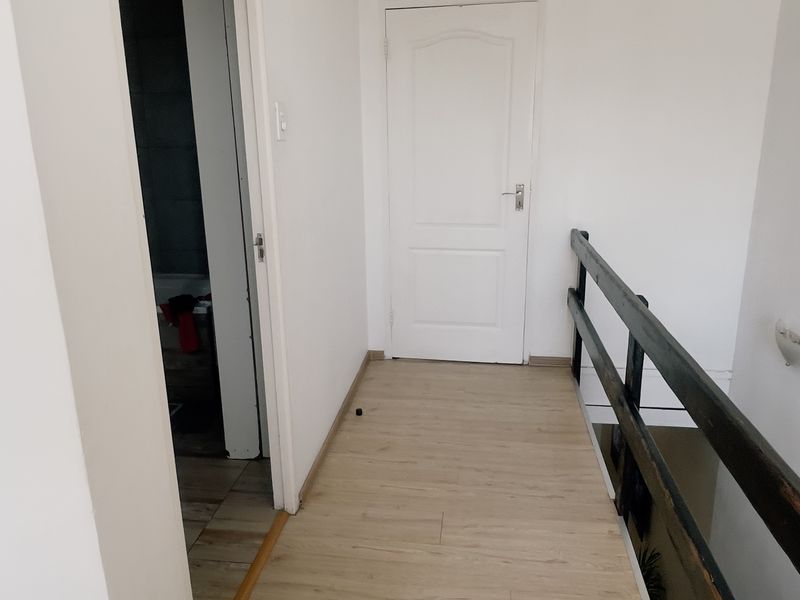 A bright, empty hallway featuring light wood-look laminate flooring and a dark timber staircase railing leading to an internal door.