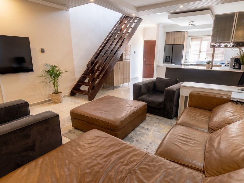 Spacious open-plan living area featuring a modern kitchen with island, tiled flooring, and a prominent wooden staircase leading to the upper level.
