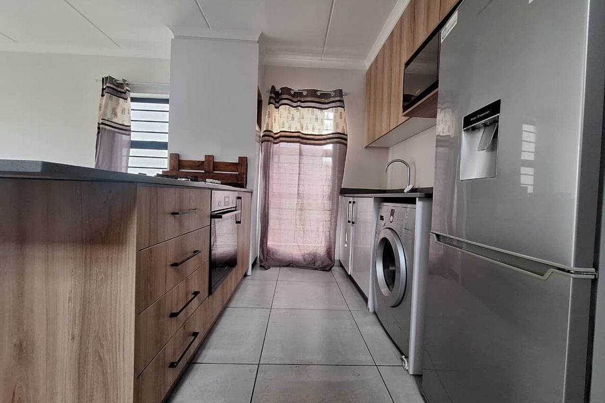 Modern kitchen featuring wood-finish cabinetry, laminate countertops, built-in oven, hob, and tiled flooring with a clean, functional layout.