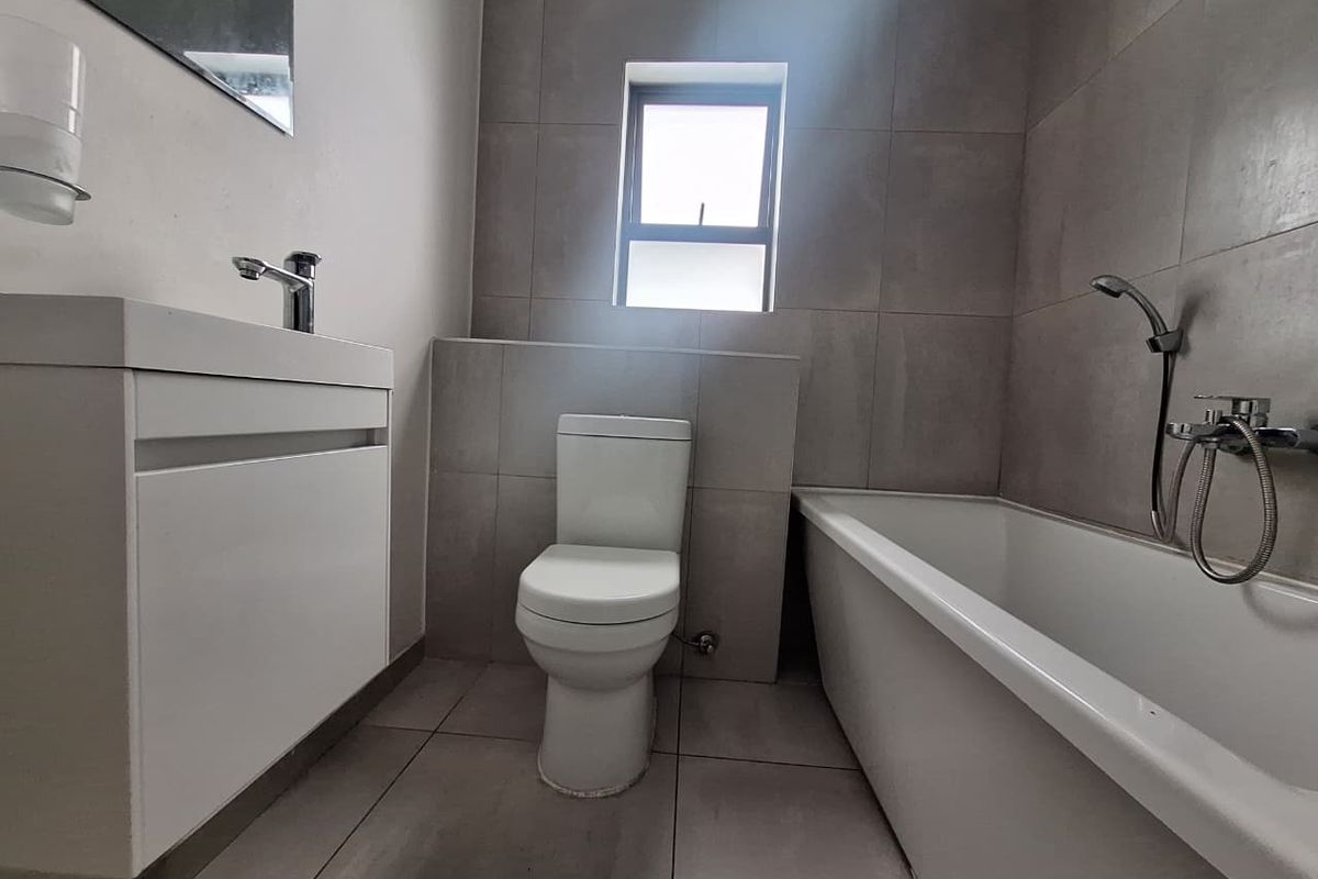 A modern, neutral-toned bathroom featuring a vanity with basin, a toilet, and a bathtub with a handheld shower attachment.