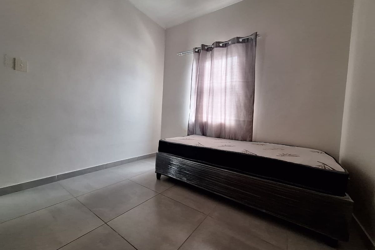 A simple, neutrally painted bedroom featuring large floor tiles and a window with a curtain rod.