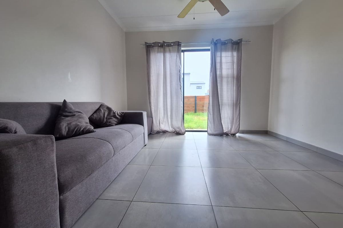 A bright living room featuring large format floor tiles, a ceiling fan, and a sliding glass door providing direct access to the rear garden.
