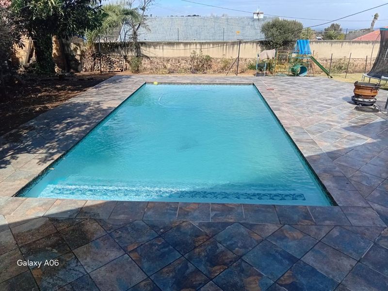 A rectangular swimming pool featuring a tiled surround and perimeter boundary wall, set within a private backyard area.
