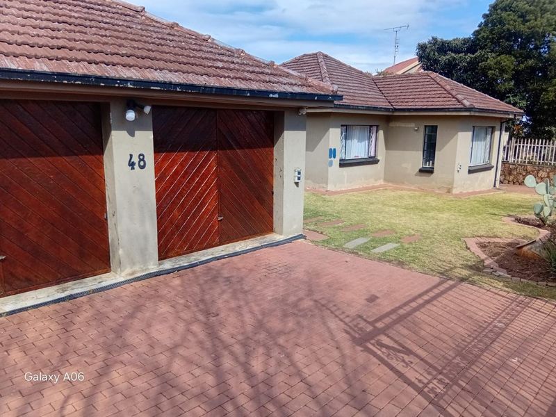 Front view of a residential property featuring a double garage with wooden doors, a paved driveway, and a small front garden.