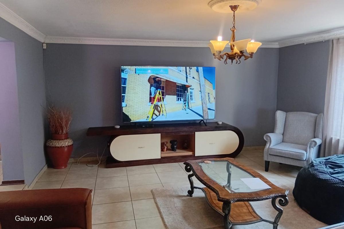 A comfortable living room featuring tiled flooring, decorative ceiling cornice, and a central chandelier, creating a welcoming and functional space.