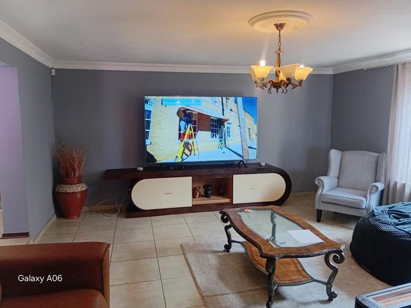A comfortable living room featuring tiled flooring, decorative ceiling cornice, and a central chandelier, creating a welcoming and functional space.