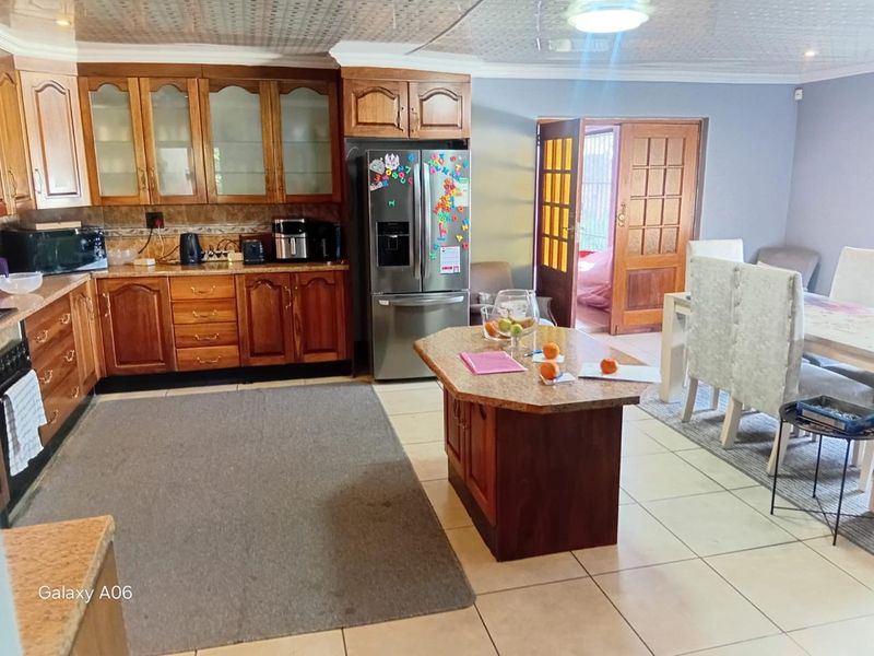 Open-plan kitchen and dining area featuring traditional wooden cabinetry, granite countertops, a central island, and tiled flooring with access to an outdoor space.