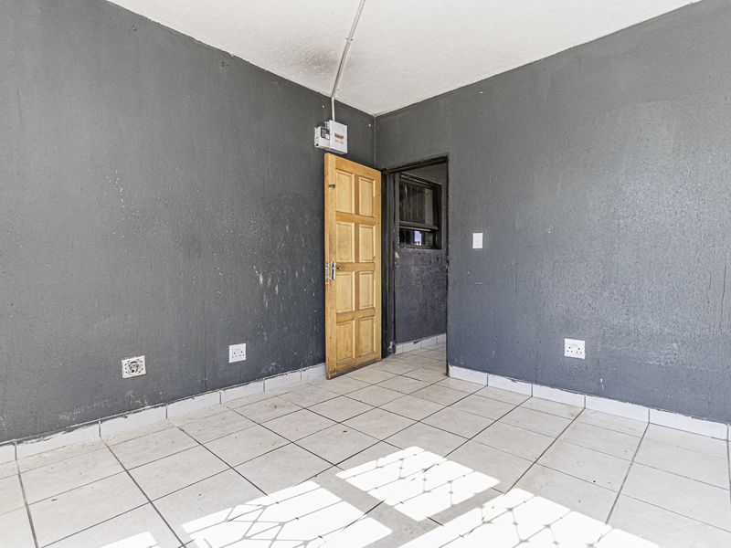 An empty bedroom featuring tiled flooring, dark grey painted walls, and a timber door with an exposed electrical distribution board.