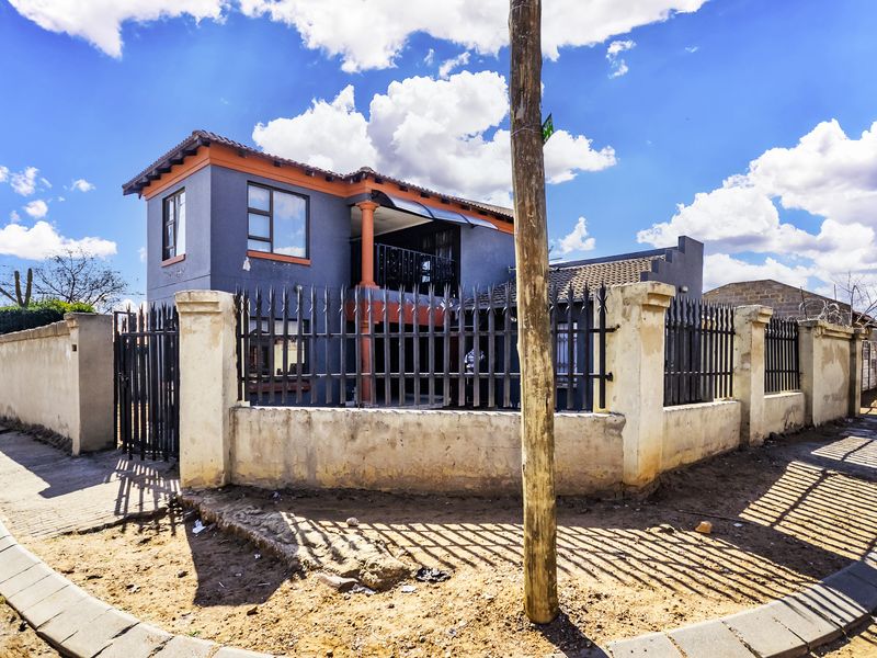Front view of a two-story house featuring a perimeter wall with metal security fencing and a balcony.