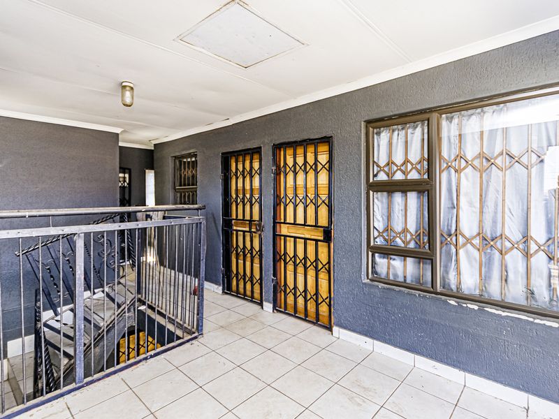 An exterior-facing hallway or landing area featuring tiled flooring, metal security gates, and a staircase with a metal balustrade.
