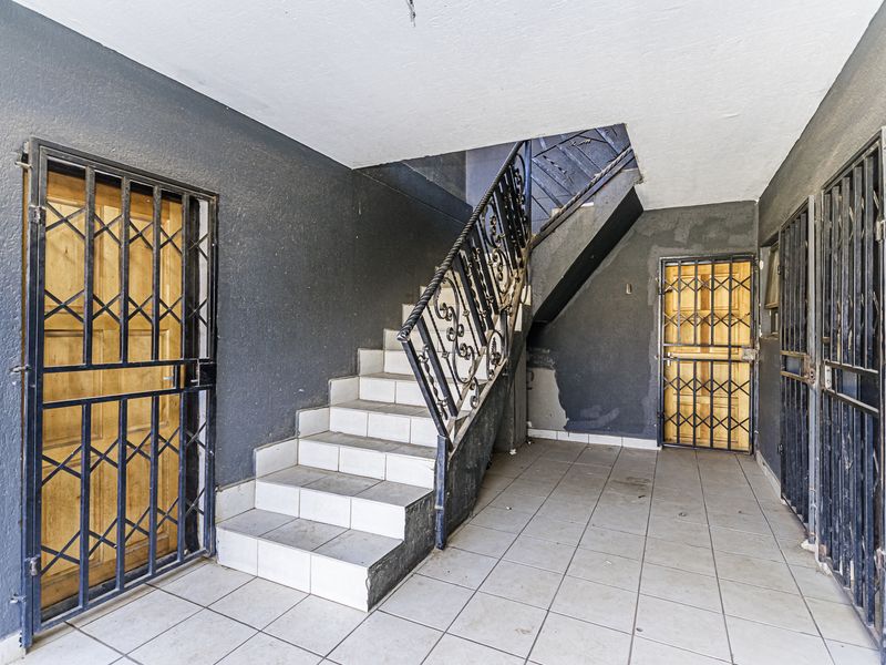 Entrance area featuring a tiled staircase with wrought iron balustrade and multiple security gates, requiring cosmetic attention to wall finishes.