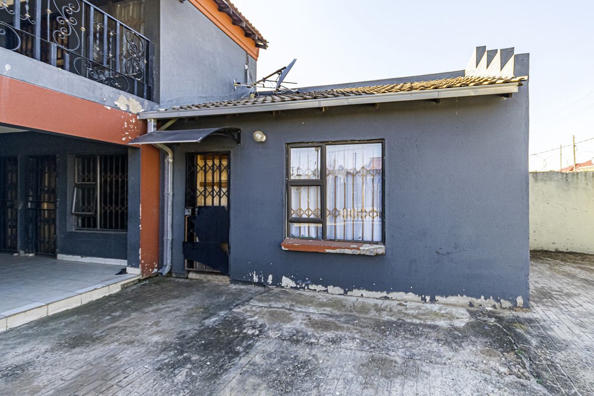 Rear exterior view of the property showing a paved area, security gates, and visible wear to the exterior wall paint and window sills.