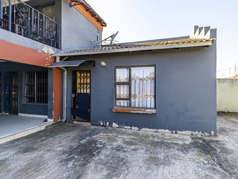 Rear exterior view of the property showing a paved area, security gates, and visible wear to the exterior wall paint and window sills.