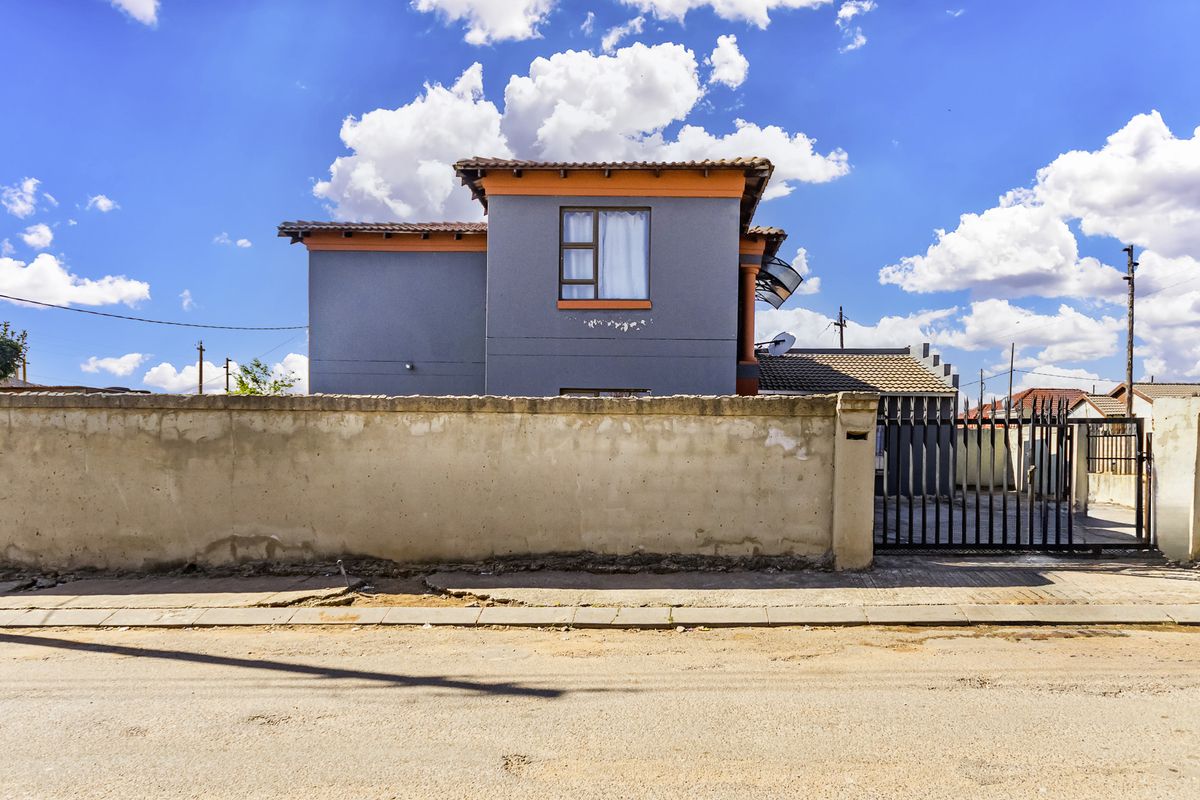 Front view of a two-story residential property featuring a perimeter boundary wall, metal gate, and tiled roof structure.