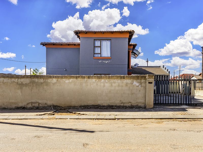 Front view of a two-story residential property featuring a perimeter boundary wall, metal gate, and tiled roof structure.