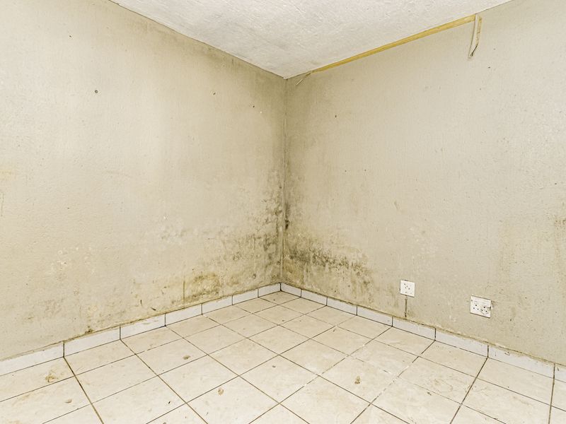 An empty bedroom featuring tiled flooring and electrical outlets, currently showing significant signs of damp and wall surface deterioration requiring maintenance.