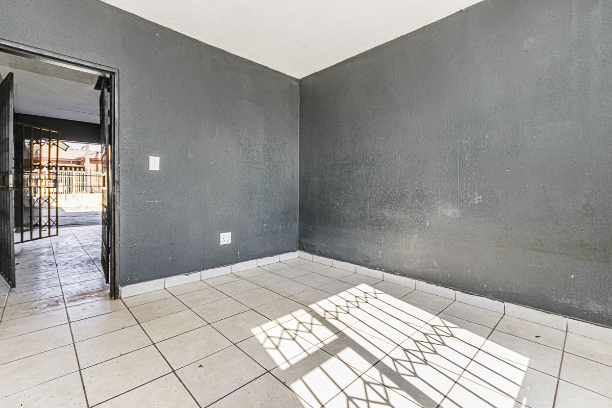 An empty living area featuring ceramic floor tiles and dark grey walls, with direct access to an exterior security gate.