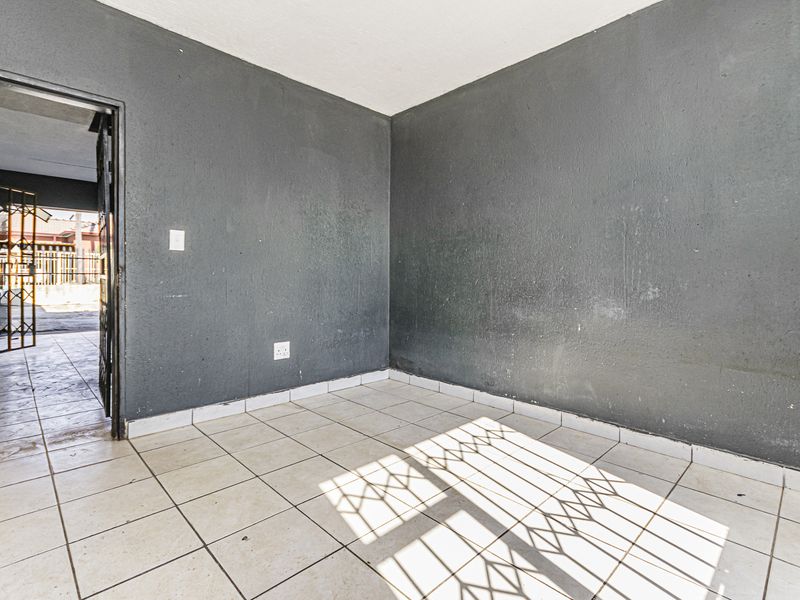 An empty living area featuring ceramic floor tiles and dark grey walls, with direct access to an exterior security gate.