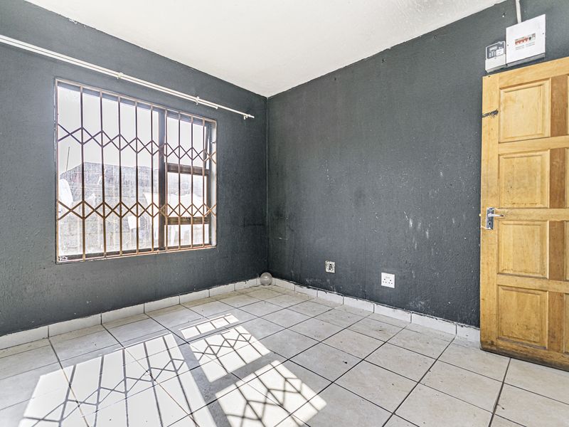 An empty bedroom featuring tiled flooring, dark painted walls, a security gate on the window, and a wooden door.