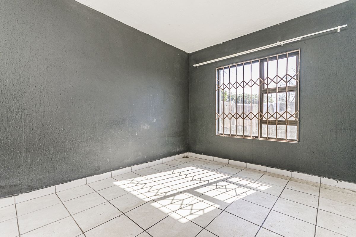An empty bedroom featuring dark painted walls, white tiled flooring, and a window fitted with a metal security gate.