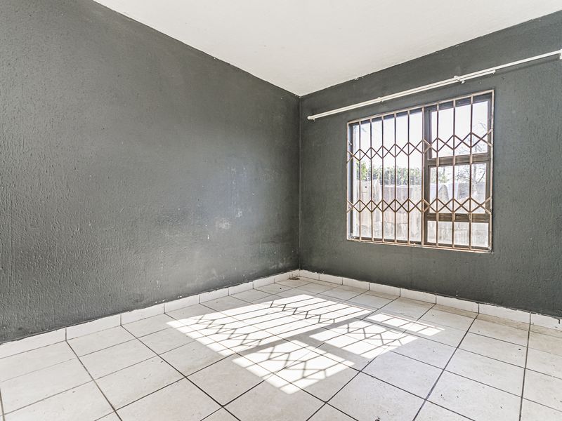 An empty bedroom featuring dark painted walls, white tiled flooring, and a window fitted with a metal security gate.