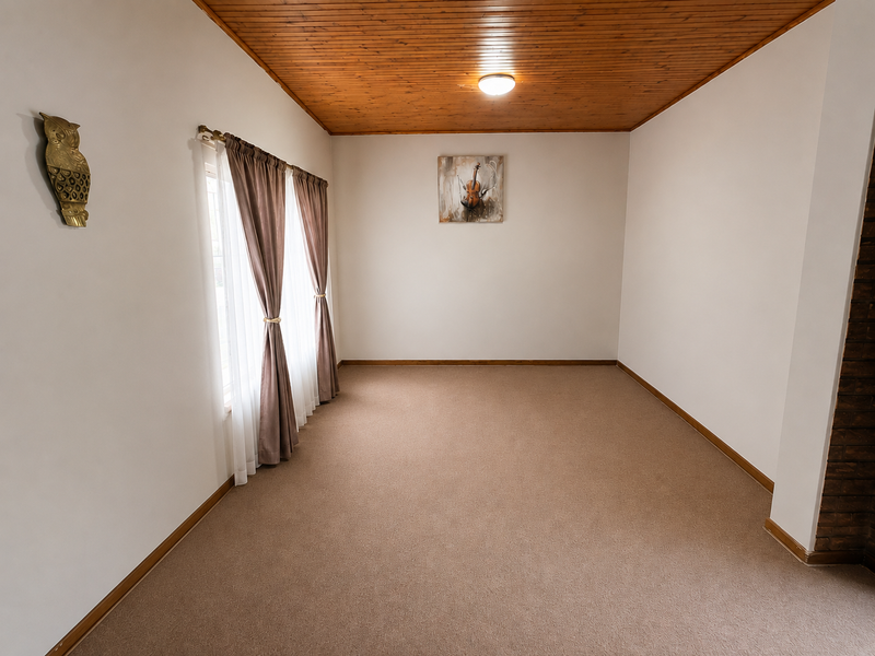 A spacious, empty living room featuring a warm timber-paneled ceiling, neutral carpeting, and large windows with curtains, offering a blank canvas for interior design.