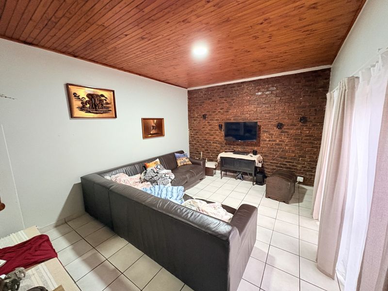 Living room featuring an exposed brick accent wall, warm timber ceiling, and neutral ceramic floor tiles.