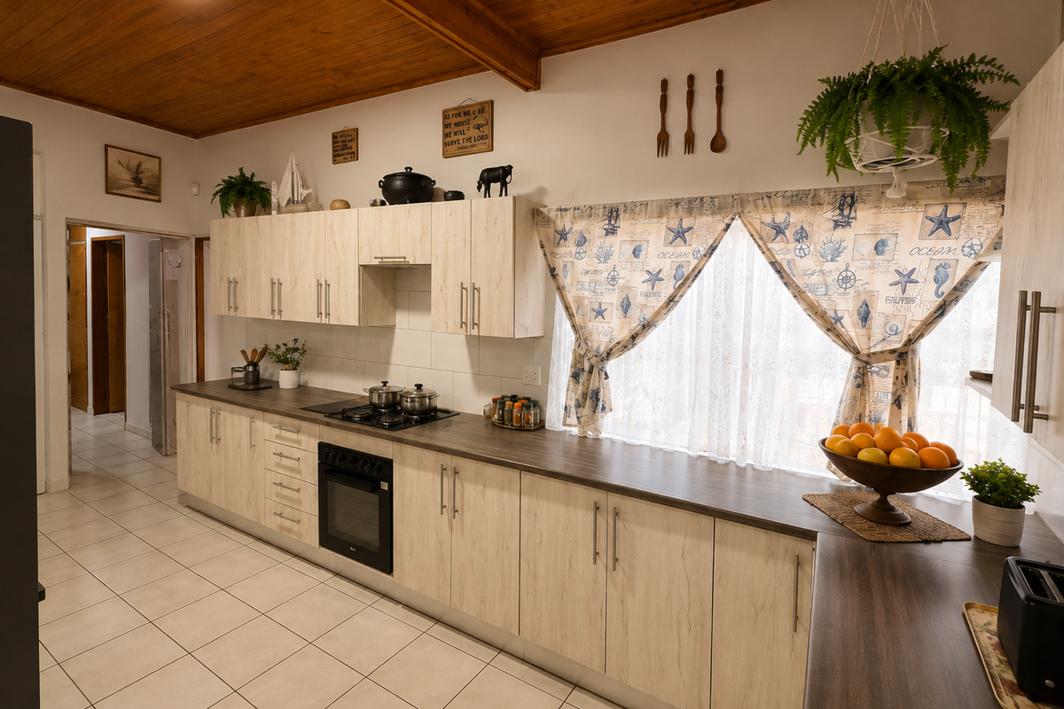A well-maintained kitchen featuring light wood-grain cabinetry, dark laminate countertops, a built-in oven with gas hob, and a warm timber-paneled ceiling.