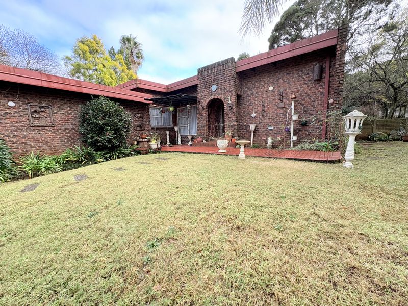 A rear view of the house featuring a face brick facade, a covered patio area, and a well-maintained garden.