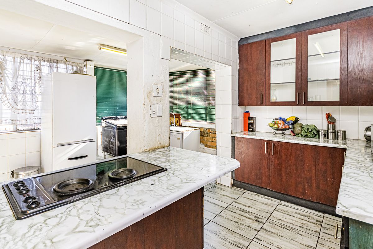 A dated kitchen featuring dark wood cabinetry, laminate countertops, and an electric hob, with visible wear and exposed brickwork requiring renovation.