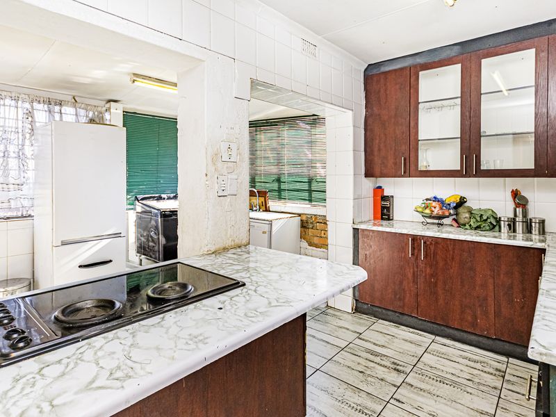 A dated kitchen featuring dark wood cabinetry, laminate countertops, and an electric hob, with visible wear and exposed brickwork requiring renovation.