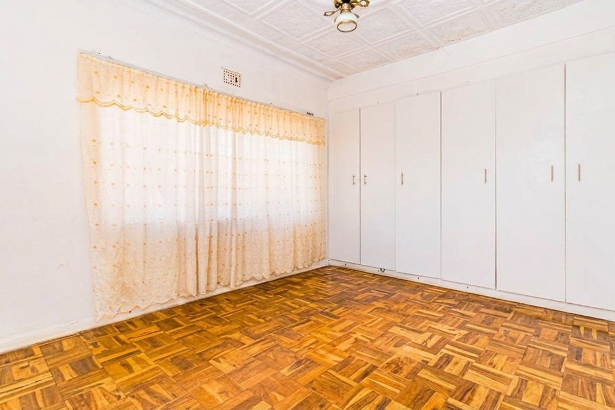 A bright, empty bedroom featuring classic parquet flooring, extensive built-in cupboards, and a decorative pressed metal ceiling.