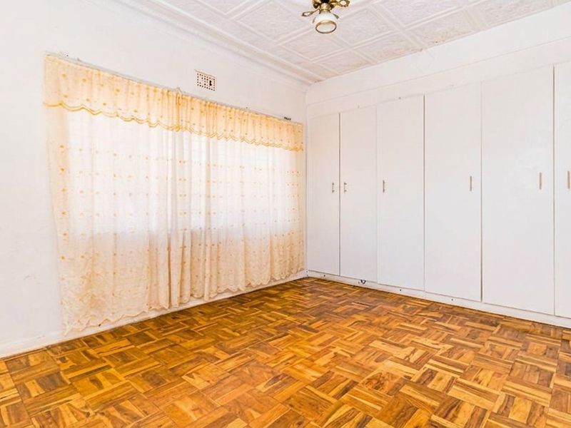 A bright, empty bedroom featuring classic parquet flooring, extensive built-in cupboards, and a decorative pressed metal ceiling.