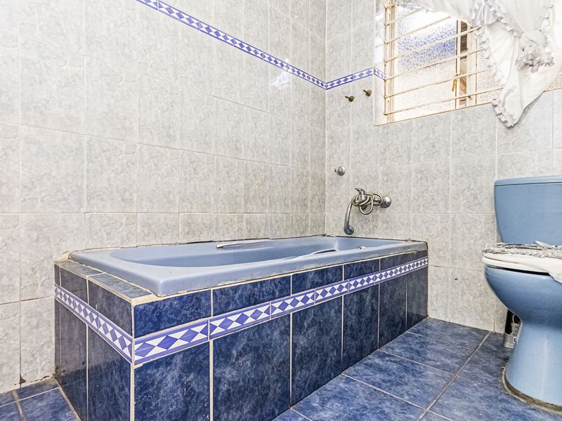 A dated bathroom featuring blue sanitary ware, tiled walls and flooring, and a built-in bathtub with a window security grille.