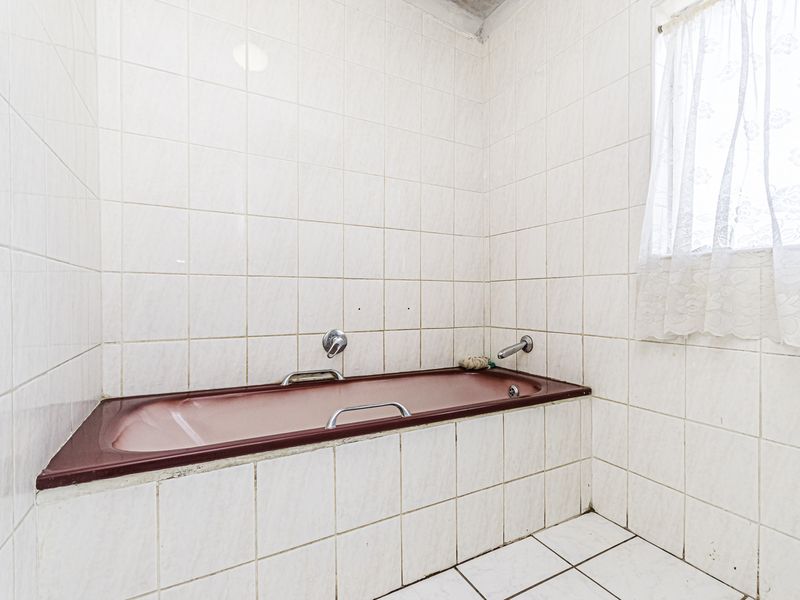 A functional bathroom featuring a built-in bathtub with chrome fixtures, surrounded by full-height wall tiling and tiled flooring.