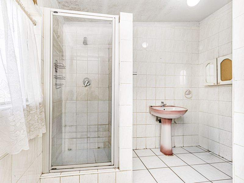A dated bathroom featuring a shower enclosure, pedestal basin, and fully tiled walls and floors, requiring cosmetic updates to modernize the space.