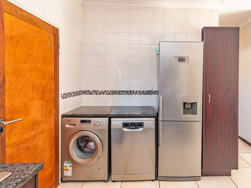 A functional laundry area featuring granite countertops, tiled splashbacks, and dedicated space for appliances with built-in cabinetry.