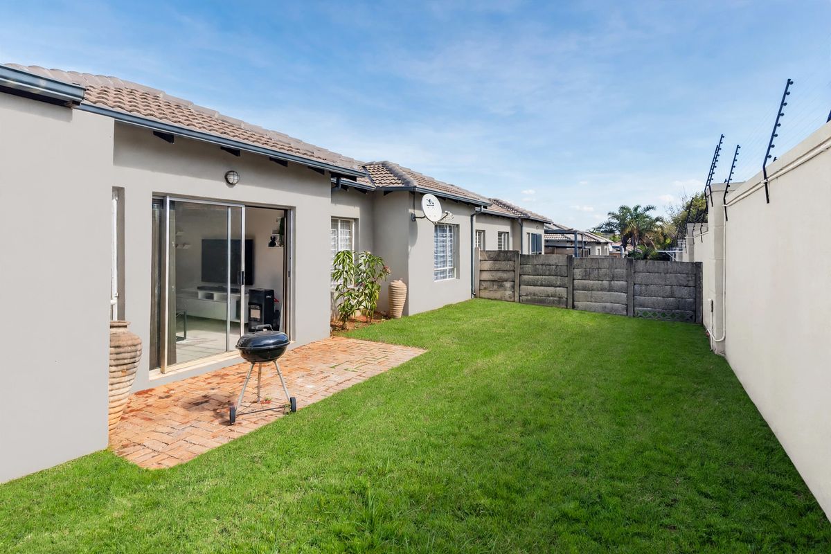 Rear view of the townhouse featuring a private garden with a brick-paved patio, lawn, and secure boundary wall with electric fencing.
