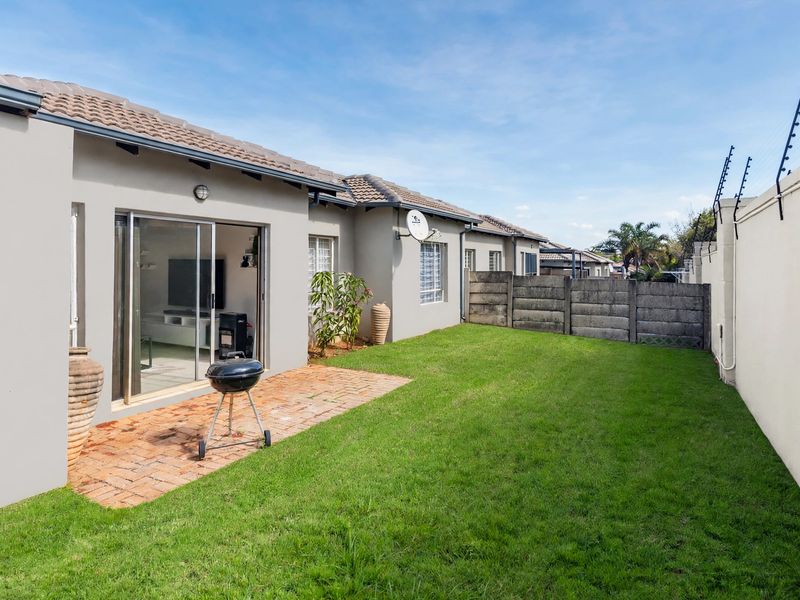 Rear view of the townhouse featuring a private garden with a brick-paved patio, lawn, and secure boundary wall with electric fencing.