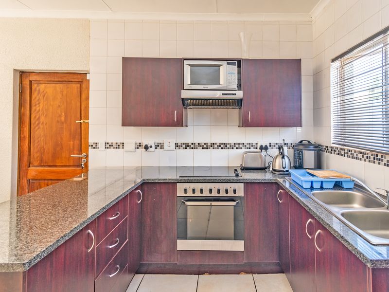 A functional kitchen featuring dark wood cabinetry, granite countertops, a built-in oven with hob, and a double stainless steel sink with tiled backsplash.