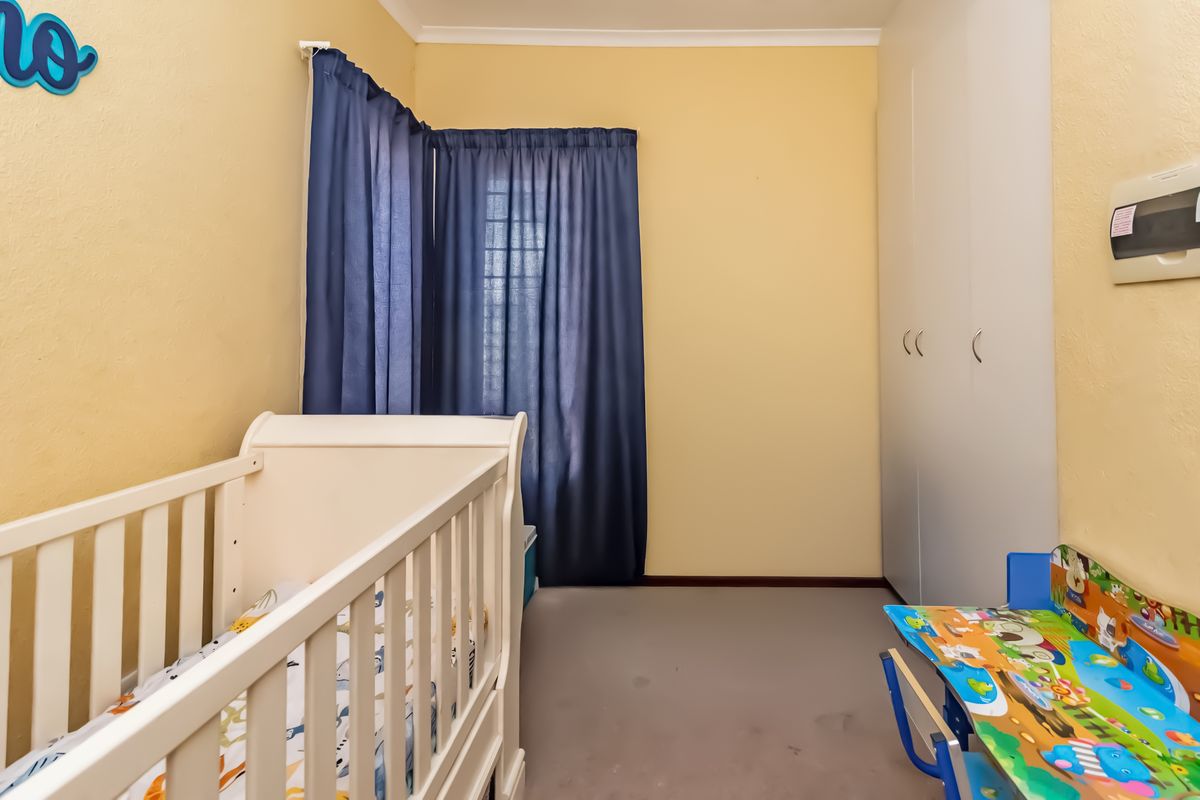 A bedroom featuring built-in cupboards, neutral wall finishes, and security bars on the window, providing a functional space for a nursery or child's room.